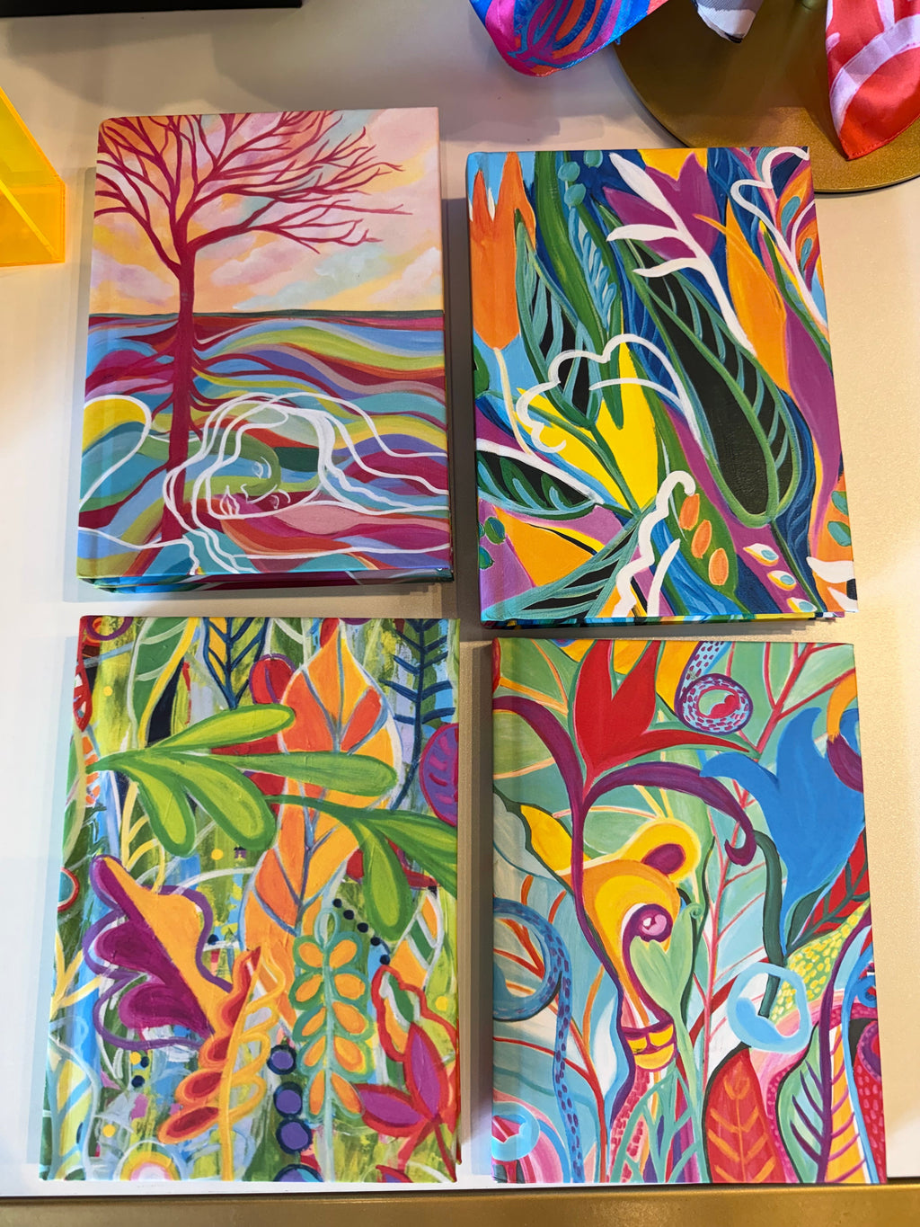 Four colorful abstract canvas paintings arranged in a 2x2 grid, featuring vibrant floral, leaf, and tree-like patterns in bright green, red, blue, yellow, orange, and purple tones.